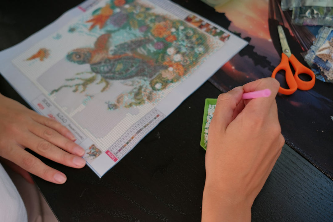 Hands placing resin diamonds onto a sea turtle diamond painting canvas